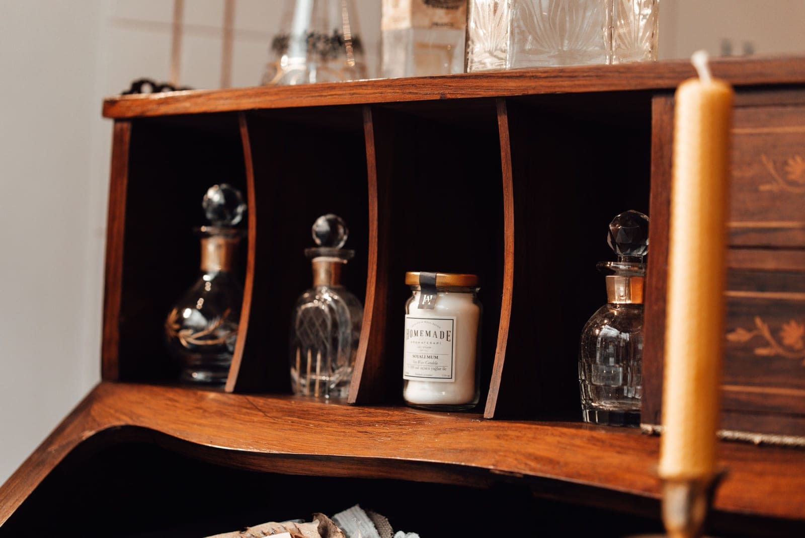 An unlit jar candle in a wooden writing-desk cubby between glass decanters