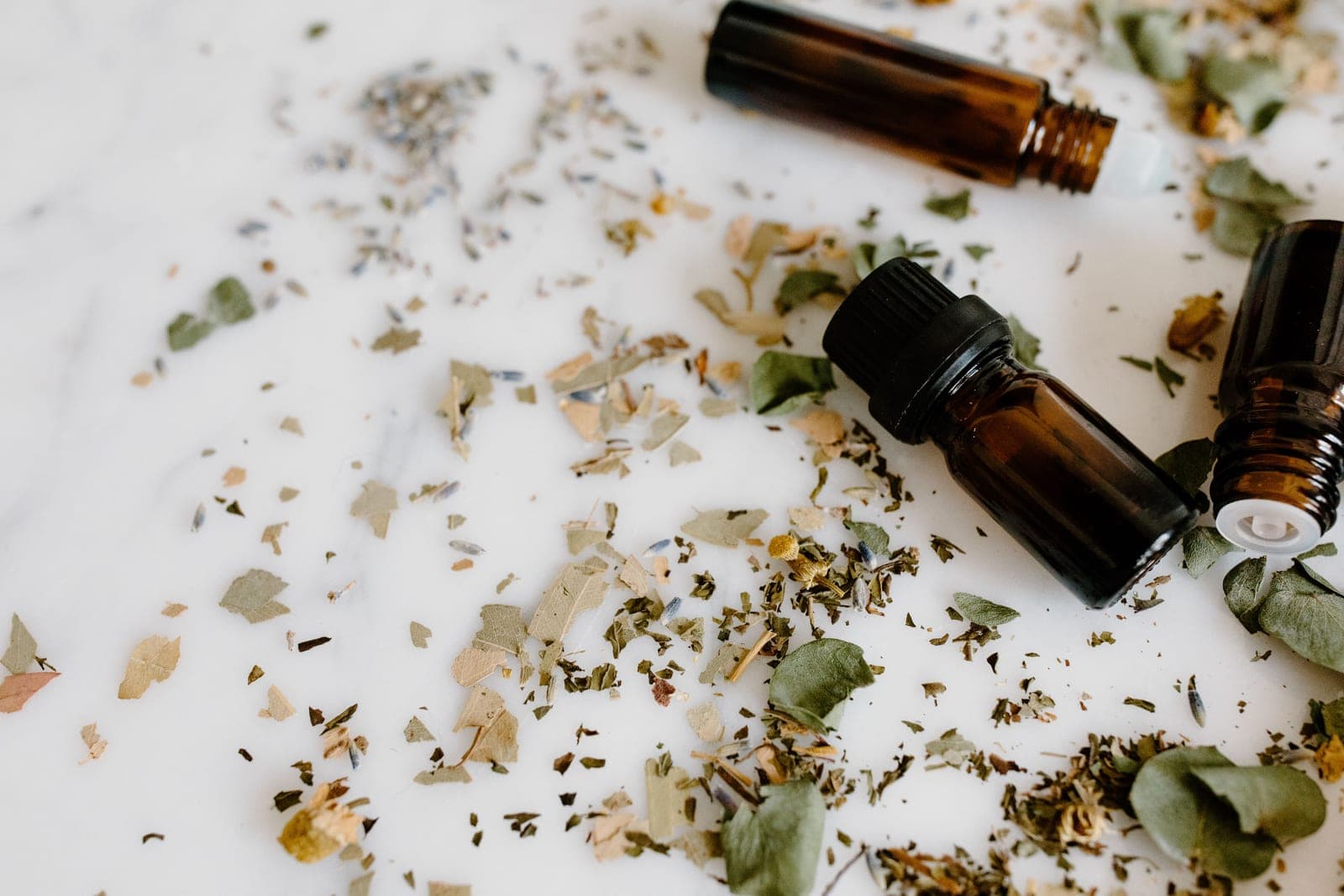 Small amber essential oil bottles and loose herbs on a white surface