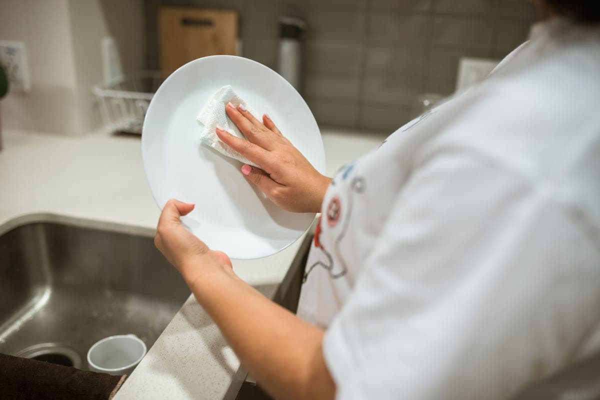 A person wiping a ceramic dish clean with a cloth