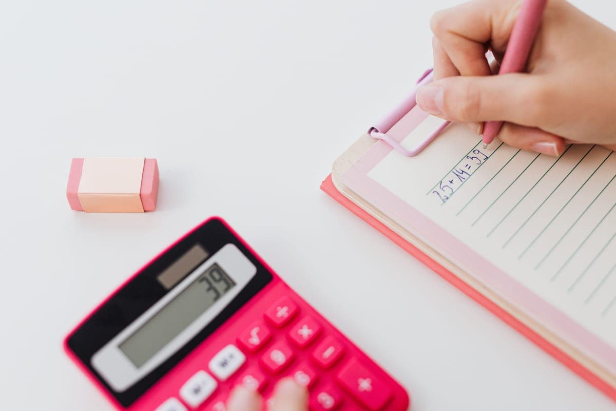 A calculator and notebook on a desk with someone writing