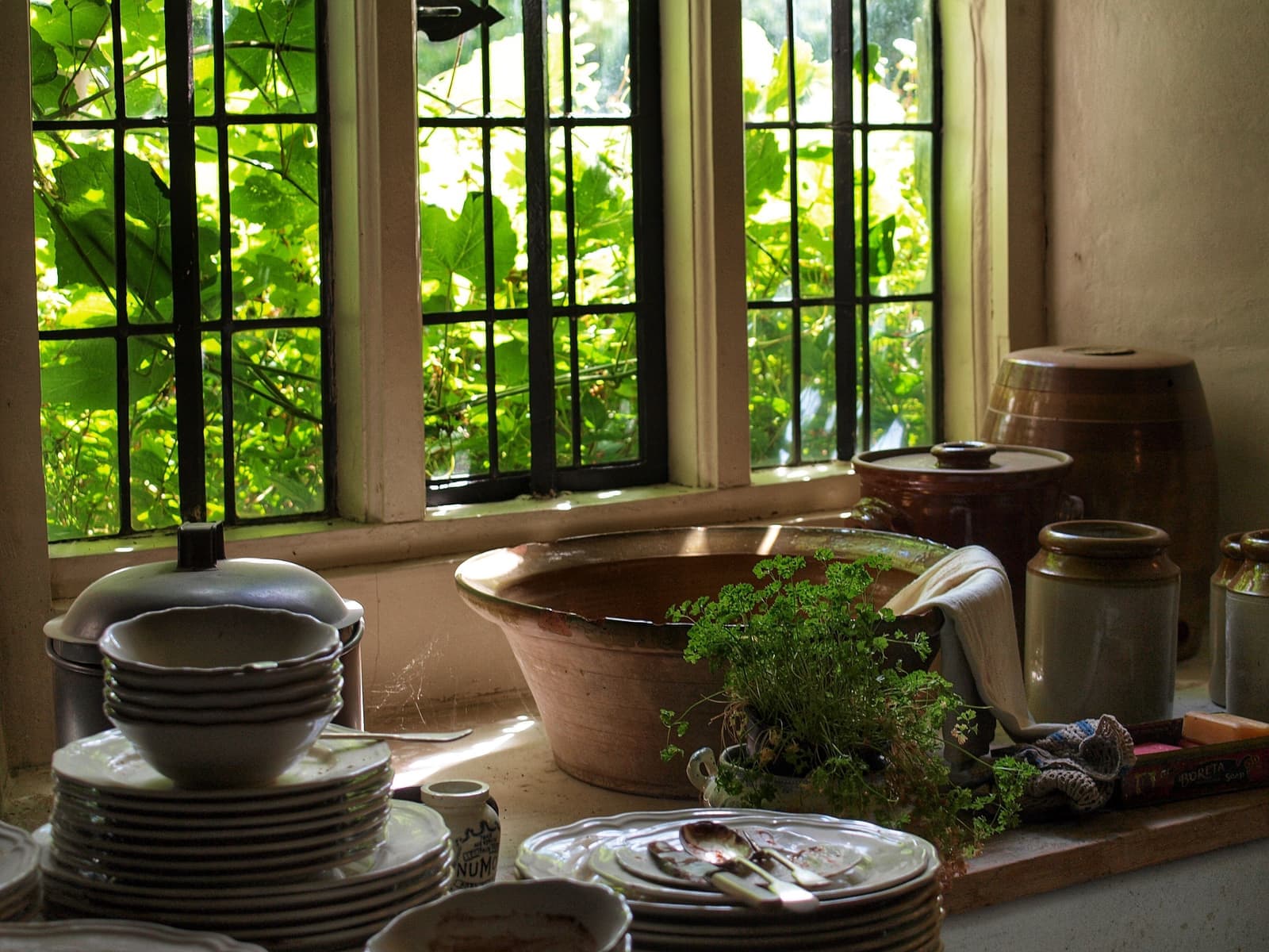 Stoneware crocks, stacked plates and herbs on a farmhouse kitchen windowsill