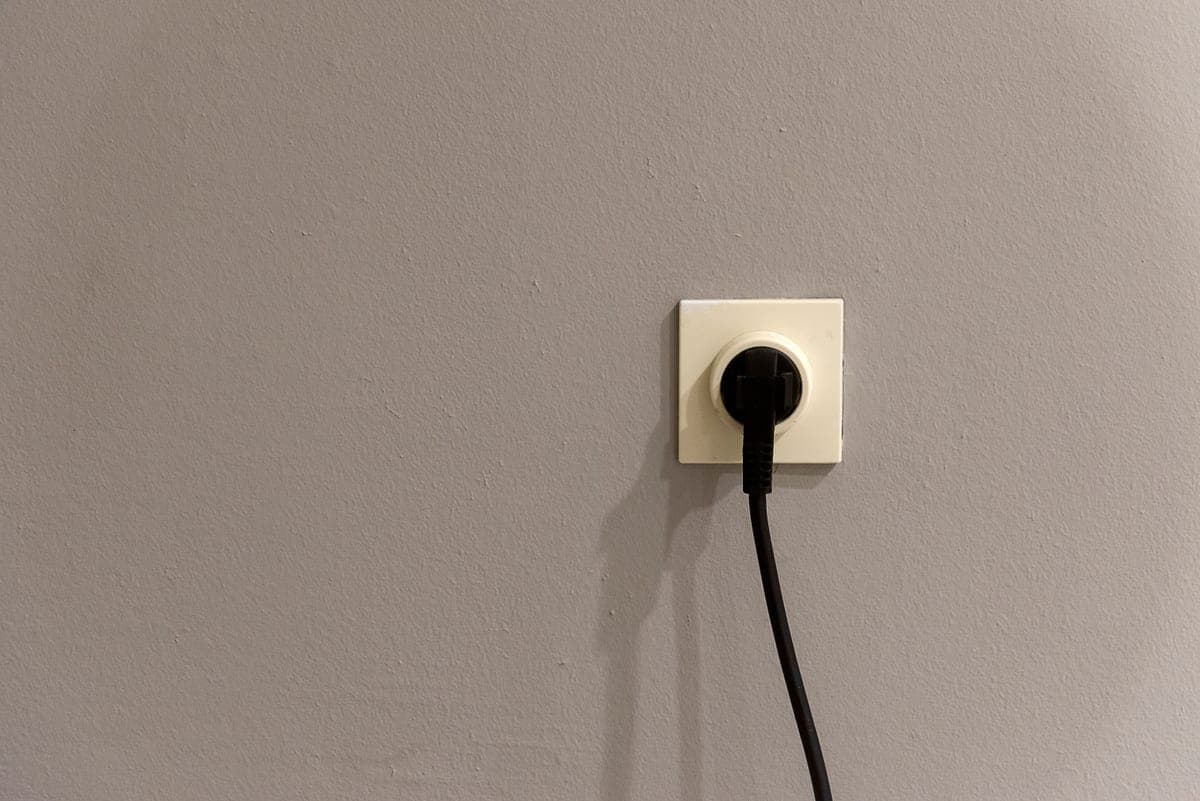 An electrical socket with a plug fitted, on a plain gray wall
