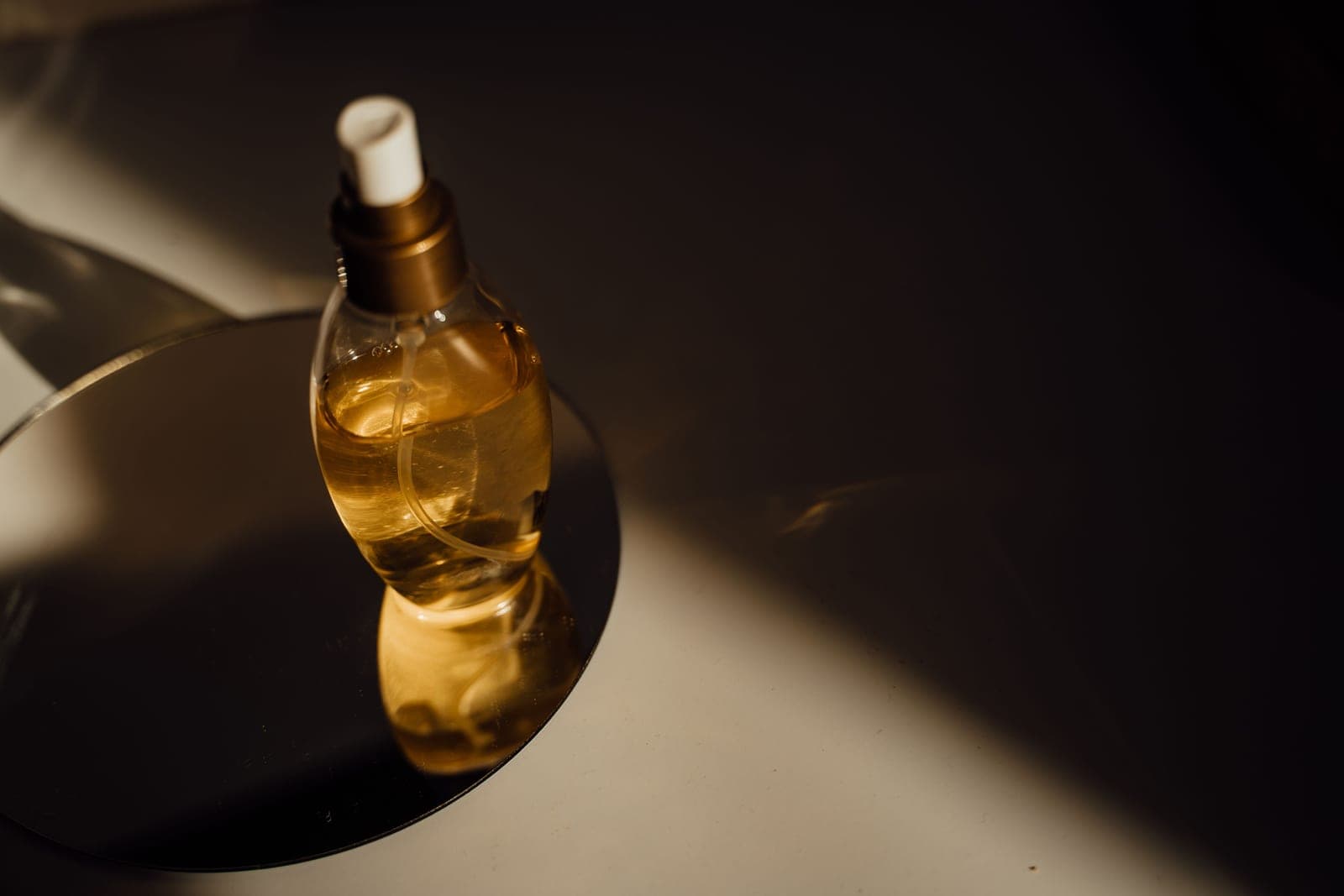 A single glass perfume bottle on a round mirror, lit from one side