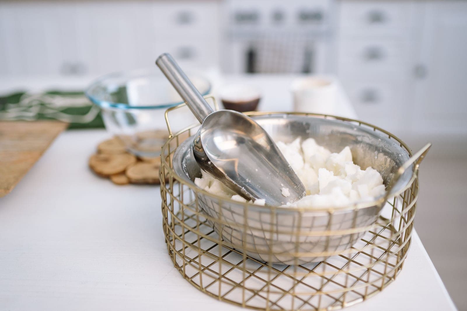 A metal bowl of white wax pieces with a scoop, on a pale kitchen counter